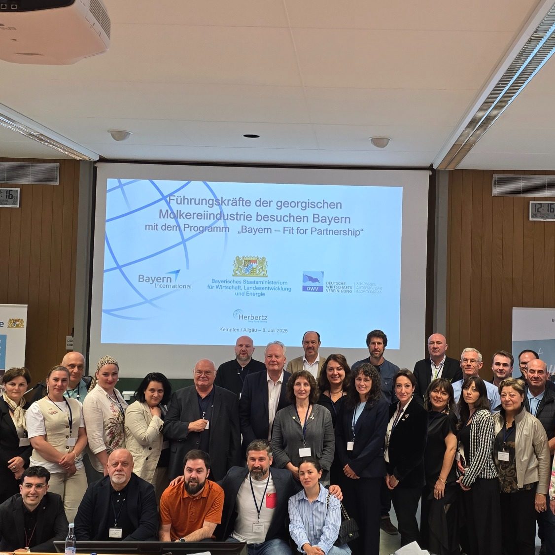 Gruppenfoto von Teilnehmern einer Konferenz, mit Präsentation im Hintergrund.